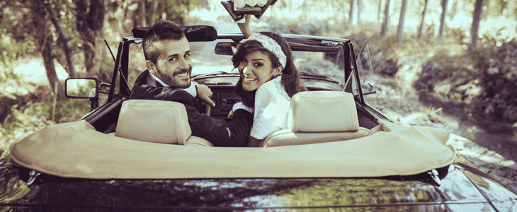 a bride and groom drive away smiling